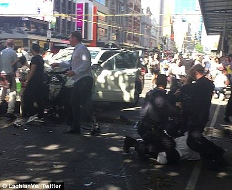 Footage shows the damaged car surrounded by dozens of injured pedestrians while police arrest the driver (pictured)