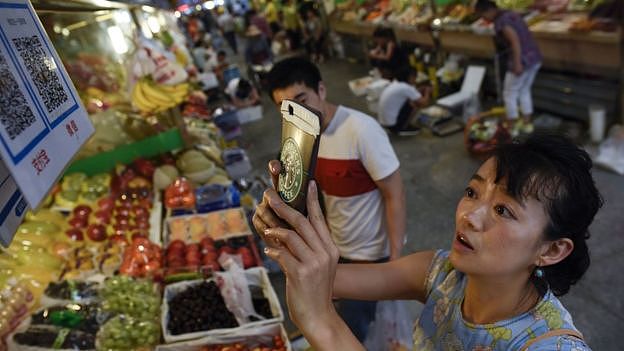 This photo taken in June 2017 shows a woman making purchases by scanning QR codes using her smartphone at a fruit stall in a market in Beijing