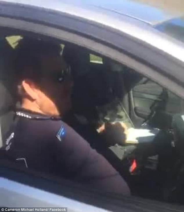 The officer, who was leaning back in the driver's seat, appeared to jump after being caught off guard (pictured) by Cameron Holland and opened the window claiming he 'just dropped off'