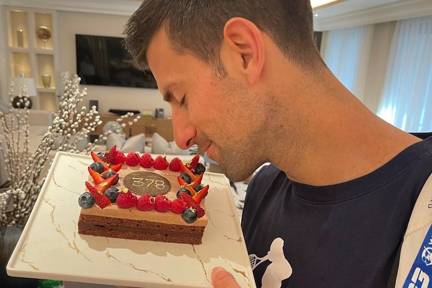 Novak Djokovic 深情地看着上面有 378 的蛋糕，庆祝他成为世界第一的周数。