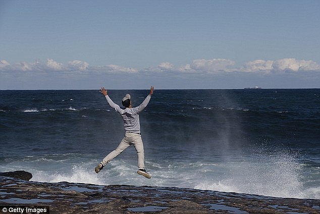 A man attempts a 'jump shot' while on slippery rocks as huge waves smash the coast around NSW