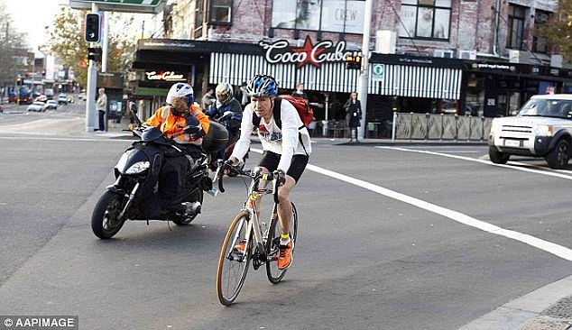 A cyclist and motorcyclist riding through the intersection of Oxford St and Flinders StÂ 
