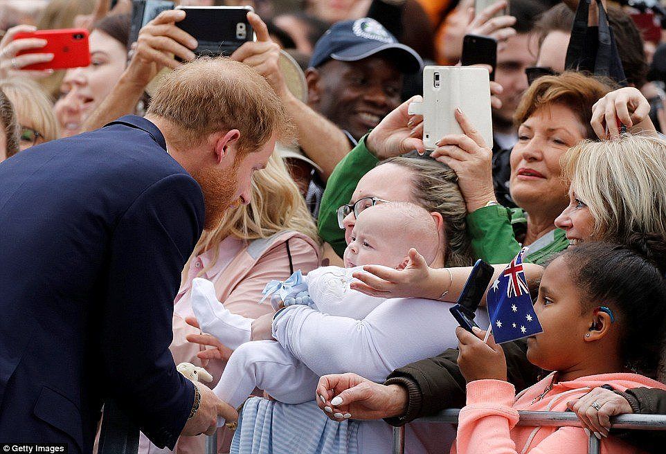 A heartwarming picture taken of Prince Harry greeting a baby as dozens of smiling fans watch on