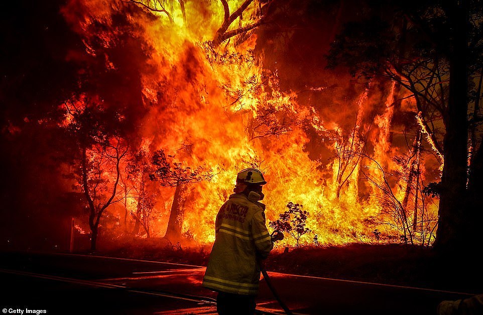 A NSW firefighter holds a hose as they prepares to extinguish a wall of flames burning near the town of Bilpin on December 19