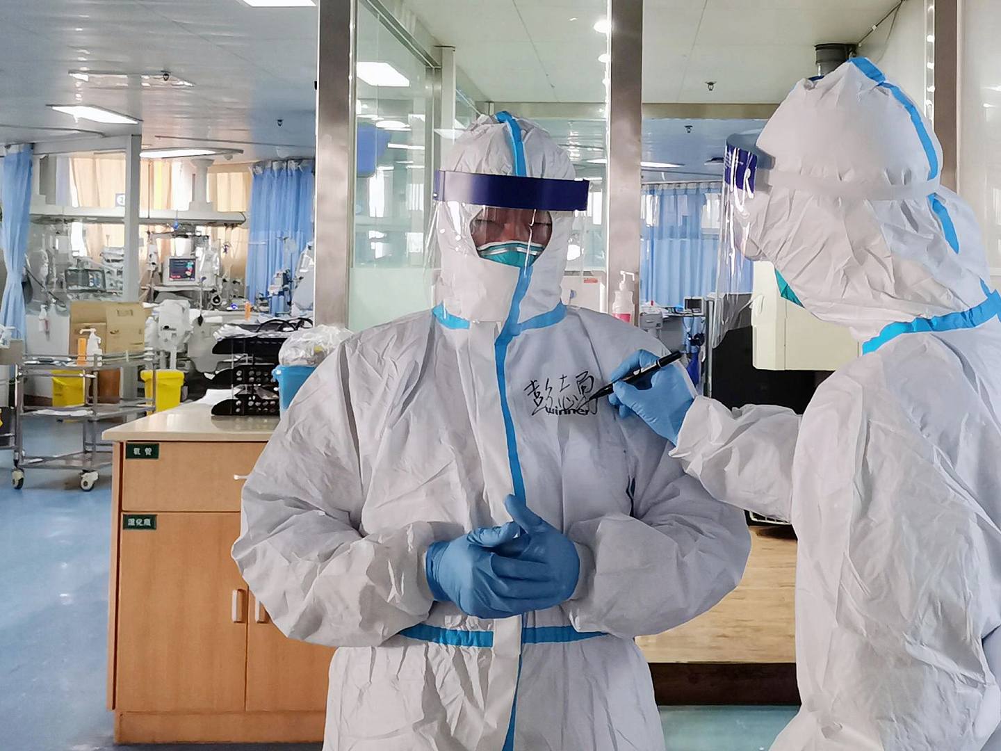 新型冠状病毒肺炎疫情在中国迅速蔓延，图为2月5日武汉大学中南医院重症医学科主任彭志勇（左）走进隔离病房准备救治患者，一名医生在他的隔离服上写下名字。（新华社）