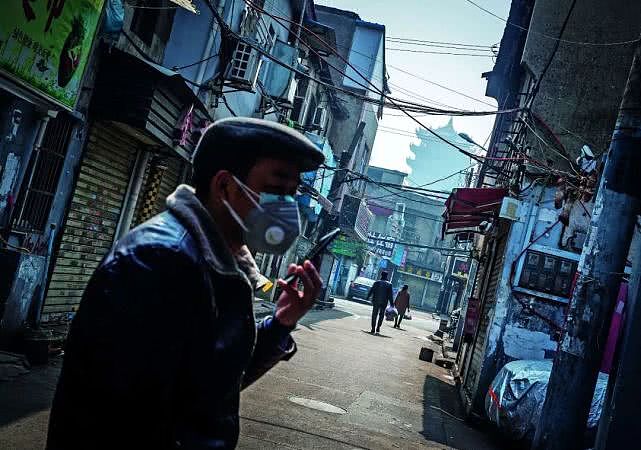 2月3日，武汉得胜桥，市民戴着口罩在小巷口打电话，远处是自古享有“天下绝景”之称的武汉标志性建筑黄鹤楼。摄影/湖北日报 柯皓