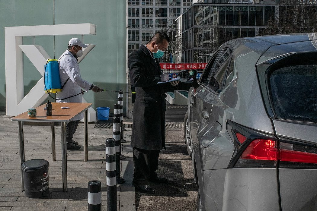 在北京一个商住小区的停车场入口，一名司机在登记、测体温，车也要经过消毒。