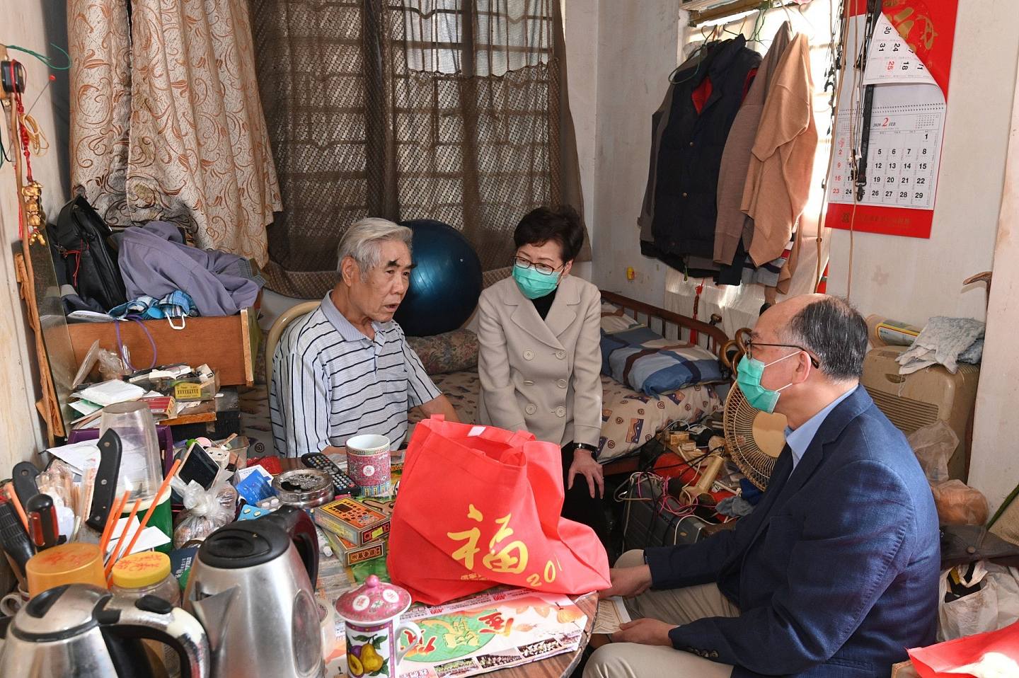 行政长官林郑月娥（中）和运输及房屋局局长陈帆（右）早前到访深水埗，向居于“劏房”的长者派发口罩等防疫用品。（HK01）