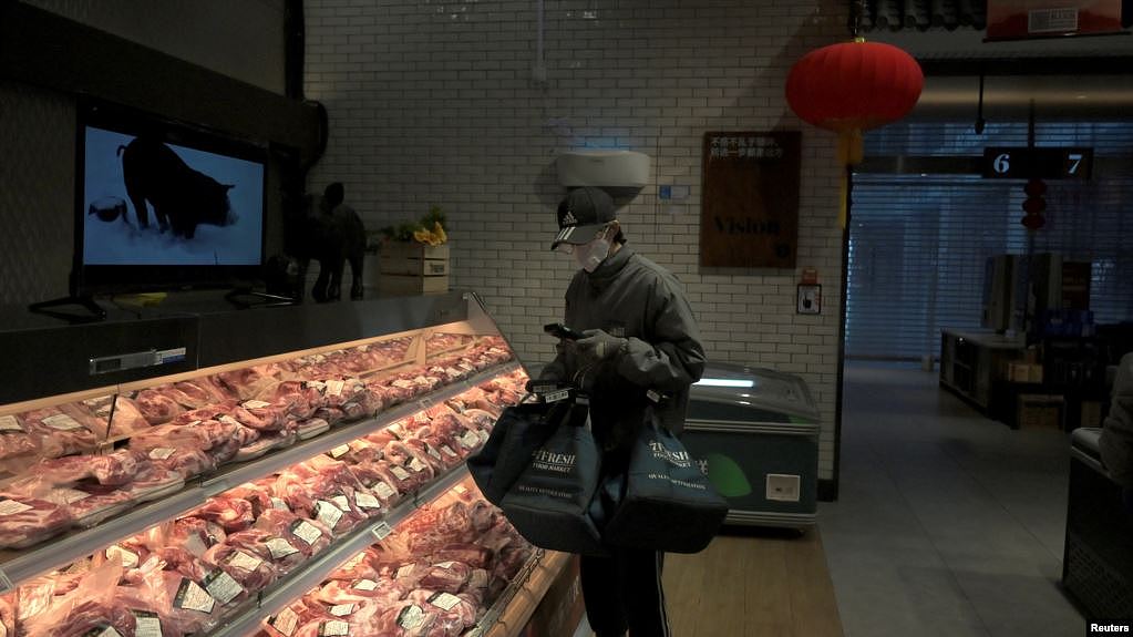 一名戴着口罩的互联网供货商在北京亦庄一家肉店为网上订户购买猪肉。（2020年2月8日）