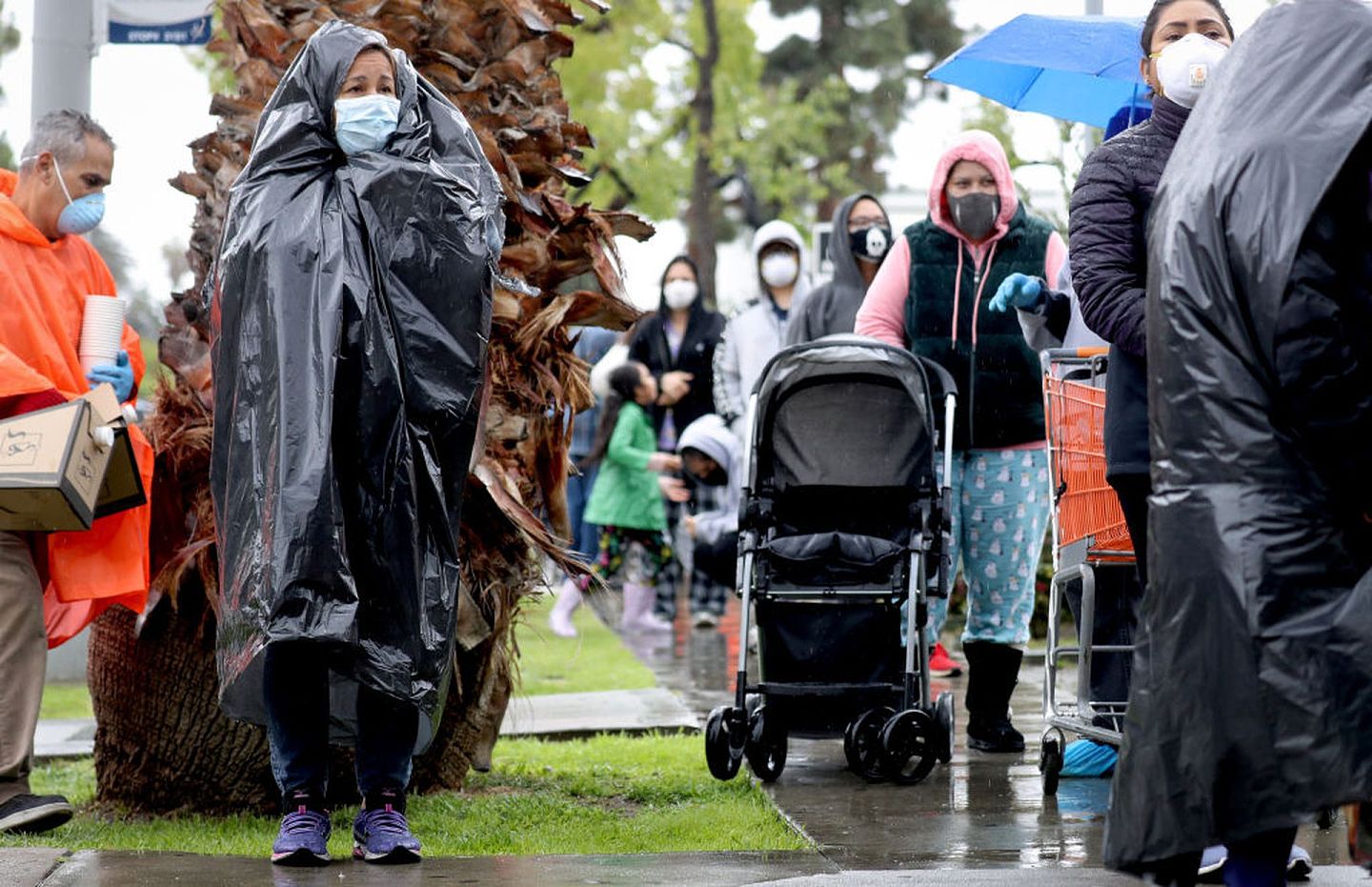 4月9日，美国加州洛杉矶市民Juana Gomez（左二）将垃圾袋当做雨衣，与其他市民一起排队等待领取食物救济。（Getty）