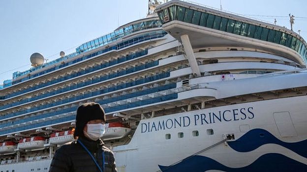 A person wearing a mask walks in front of a large cruise ship