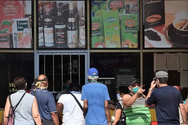 古巴从4月10日起开始关闭国内部分大型商店，但保障基础用品供应；图为4月11日，在古巴首都哈瓦那，民众戴口罩在商店窗口购买食物