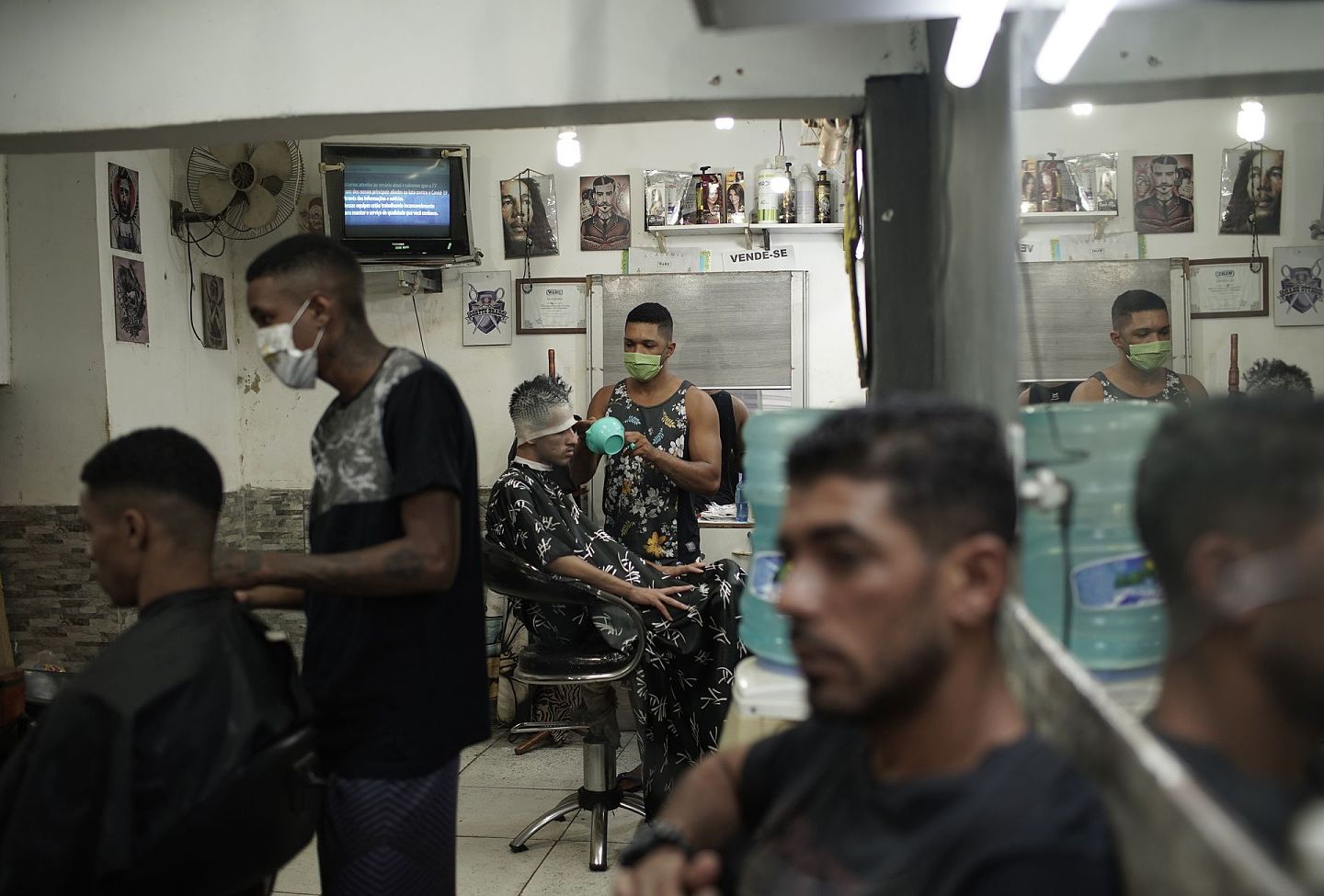 4月21日，巴西里约曼德拉贫民窟的一家理发店里，理发师们戴着防护口罩为顾客服务。（AP）