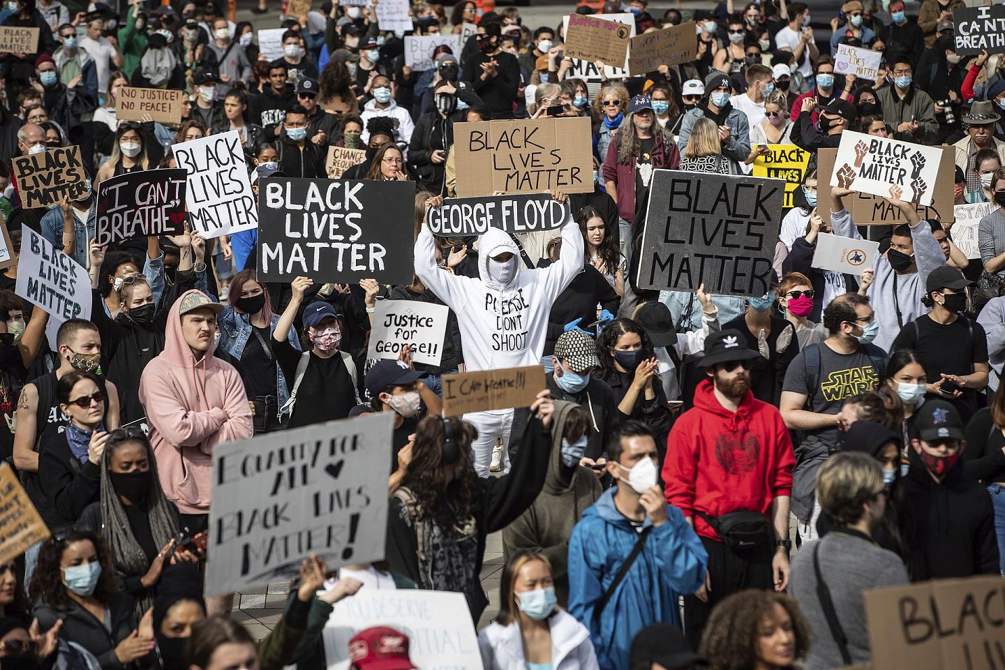 5月31日，加拿大温哥华成千上万的人聚集在一起举行和平示威，抗议种族主义、不公正和警察的暴行，一名男子举着一个写着弗洛伊德名字的滑板举过头顶。（AP）