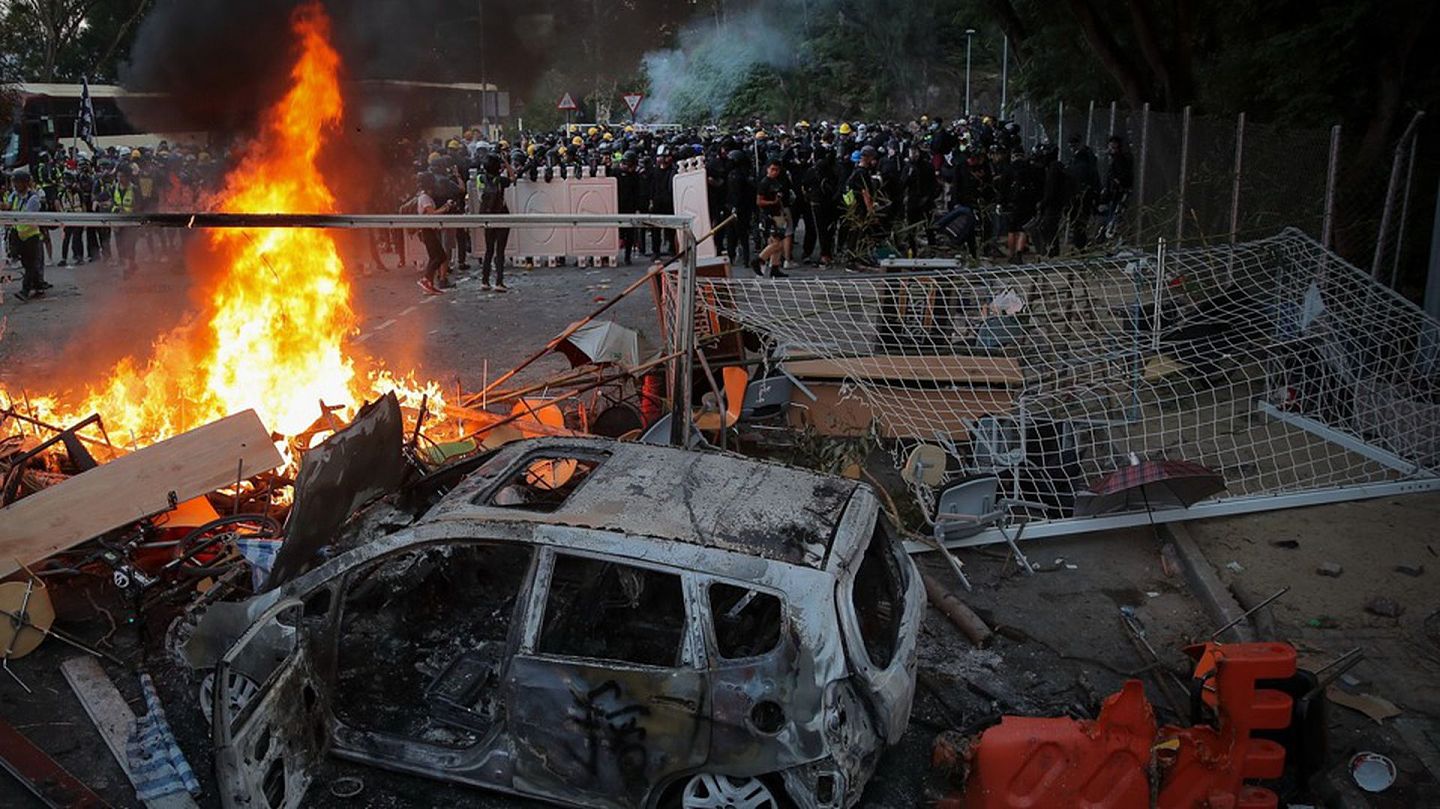 2019年11月12日，在香港中文大学与防暴警察的对峙中，学生示威者站在烧焦的车辆附近。（AP）