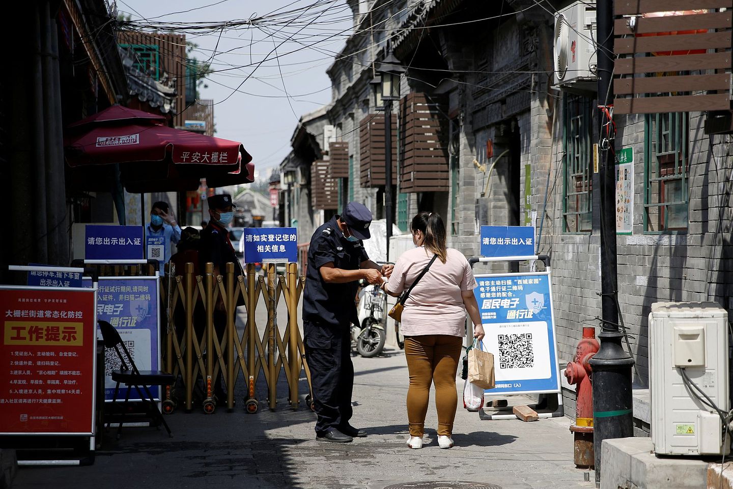 6月18日 ，带着口罩的保安在胡同入口给一名女士量体温。（Reuters）