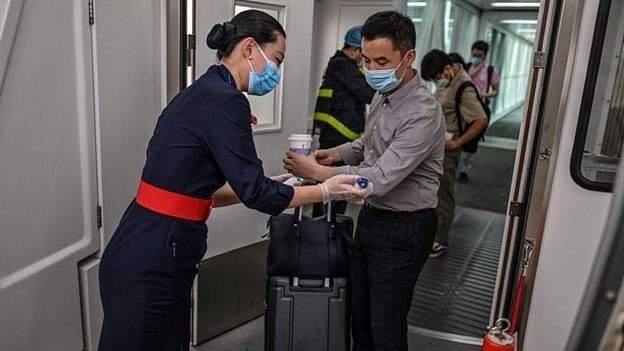 A flight attendant wearing a facemask (L) checks the body temperature of the passengers next to the door of the plane at the Tianhe Airport in Wuhan, in Chinas central Hubei province on May 29, 2020