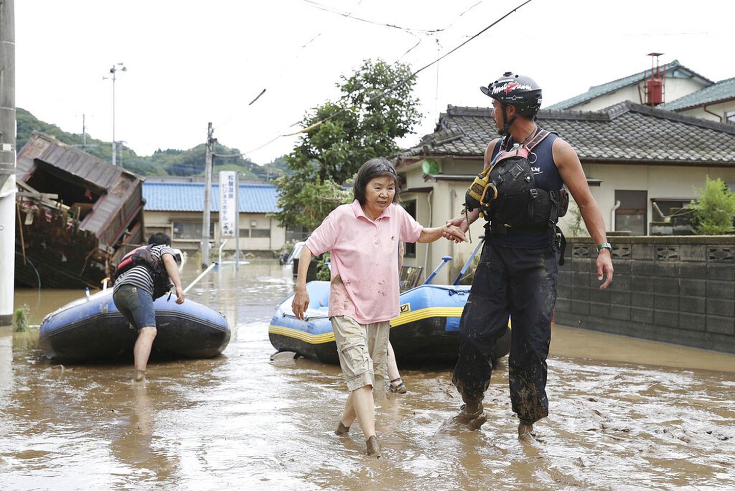人吉市一名被困的女子7月4日获救，图为救援人员牵着这名女子涉水而行。（AP）