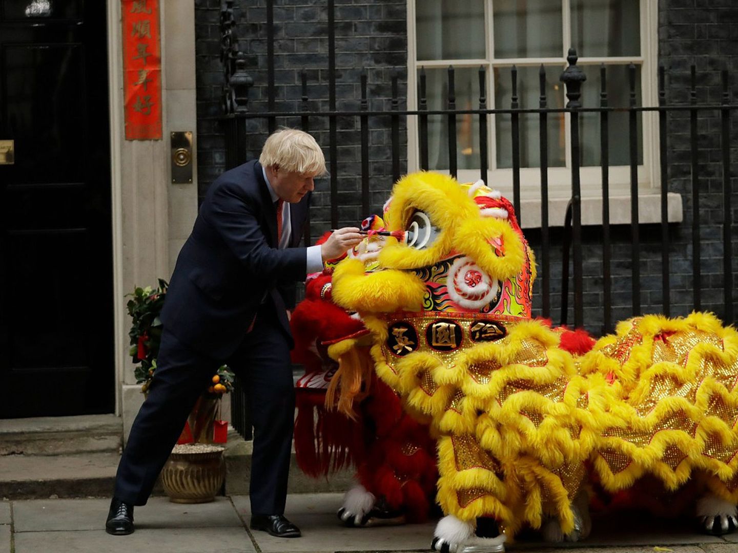1月24日，英国首相约翰逊在伦敦唐宁街10号外欢迎英国华人社区成员参加中国农历新年庆祝活动时，用画笔在表演者穿着的舞狮服装上“点睛”。（AP）