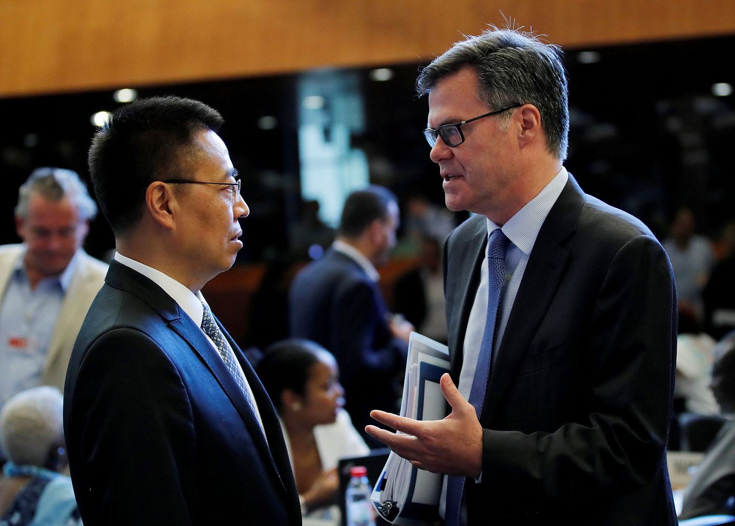 2018年7月26日，世贸组织在日内瓦总部举行总理事会会议，美国驻世贸组织代表谢伊（Dennis Shea，右）与中国驻世贸组织大使张向晨交谈。（Reuters）