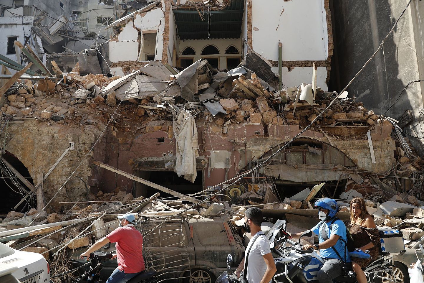 2020年8月5日，星期三，黎巴嫩贝鲁特海港，居民们骑着他们的摩托车经过在周二的大爆炸中被摧毁的房子前。（AP)