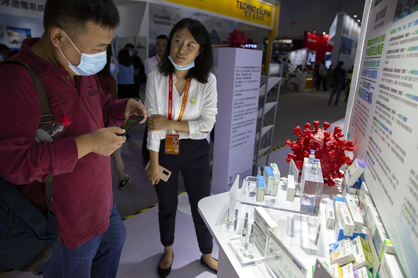 一名工作人员向参观民众介绍中国生物展出的两个新冠病毒灭活疫苗。 （AP）