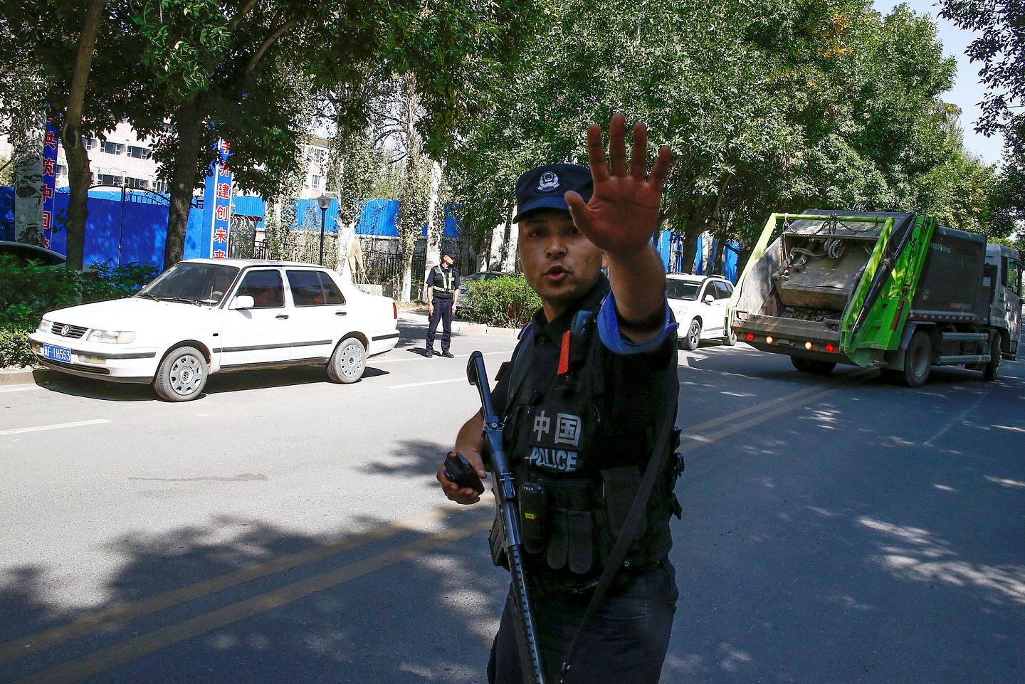 2018年9月4日，在新疆维吾尔自治区伊宁市职业教育中心附近，一名手持自动武器的中国警察在路障前向记者们做手势。（Reuters）