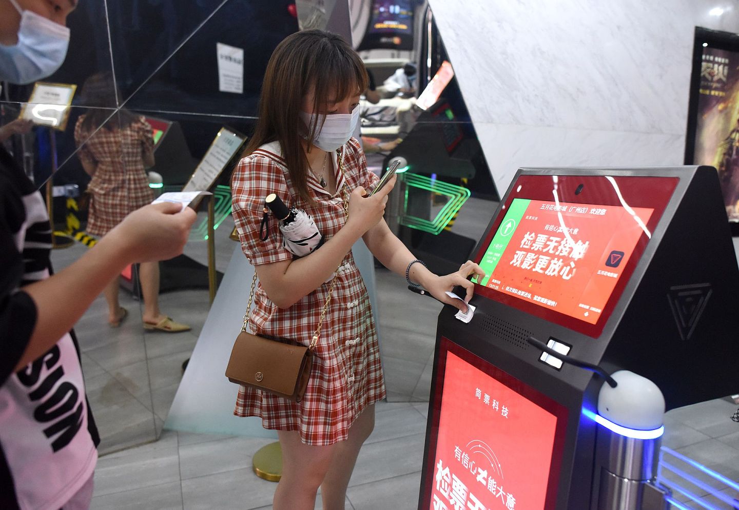 7月20日，观众在广州市五月花电影城通过扫码测温一体化的无人电子检票机扫码入场。当天，广州市部分电影院在各项疫情防控措施有效落实到位的前提下，有序恢复开放。（新华社）