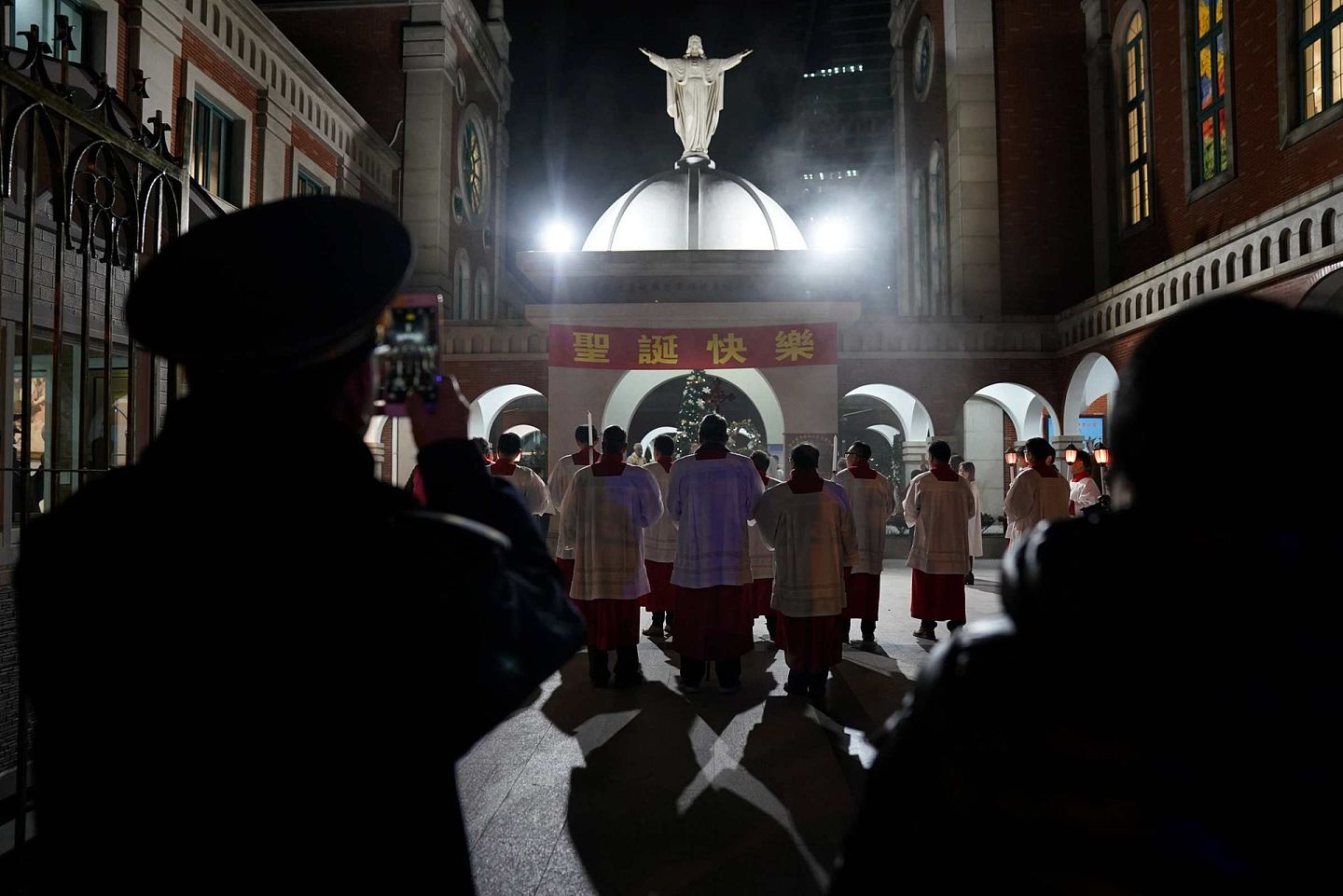 中国上海天主教徒参加圣诞节集会活动，一名警察用手机拍摄现场画面。（Reuters）