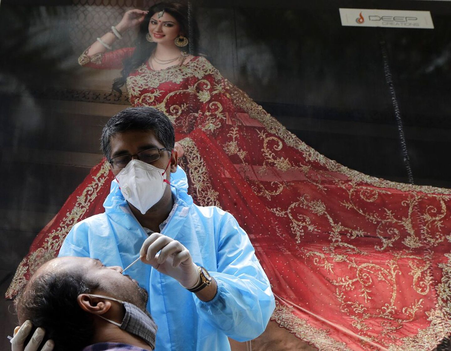 10月13日，一名医疗人员在印度孟买一间纺织品商店门外，为一名男子进行鼻拭子测试。（AP）