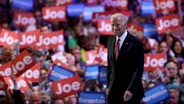 Joe Biden on stage in front of a crowd holding up signs with his name on them.