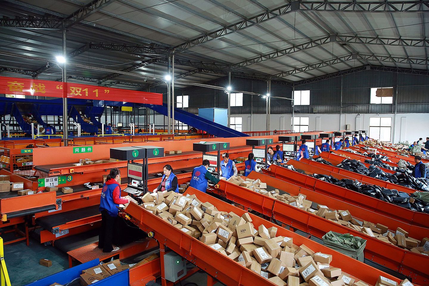 2019年11月11日下午，浙江的一处中国邮政邮件处理中心内大批包裹堆积如山，工作人员忙碌地处理着一件件快递。（视觉中国）