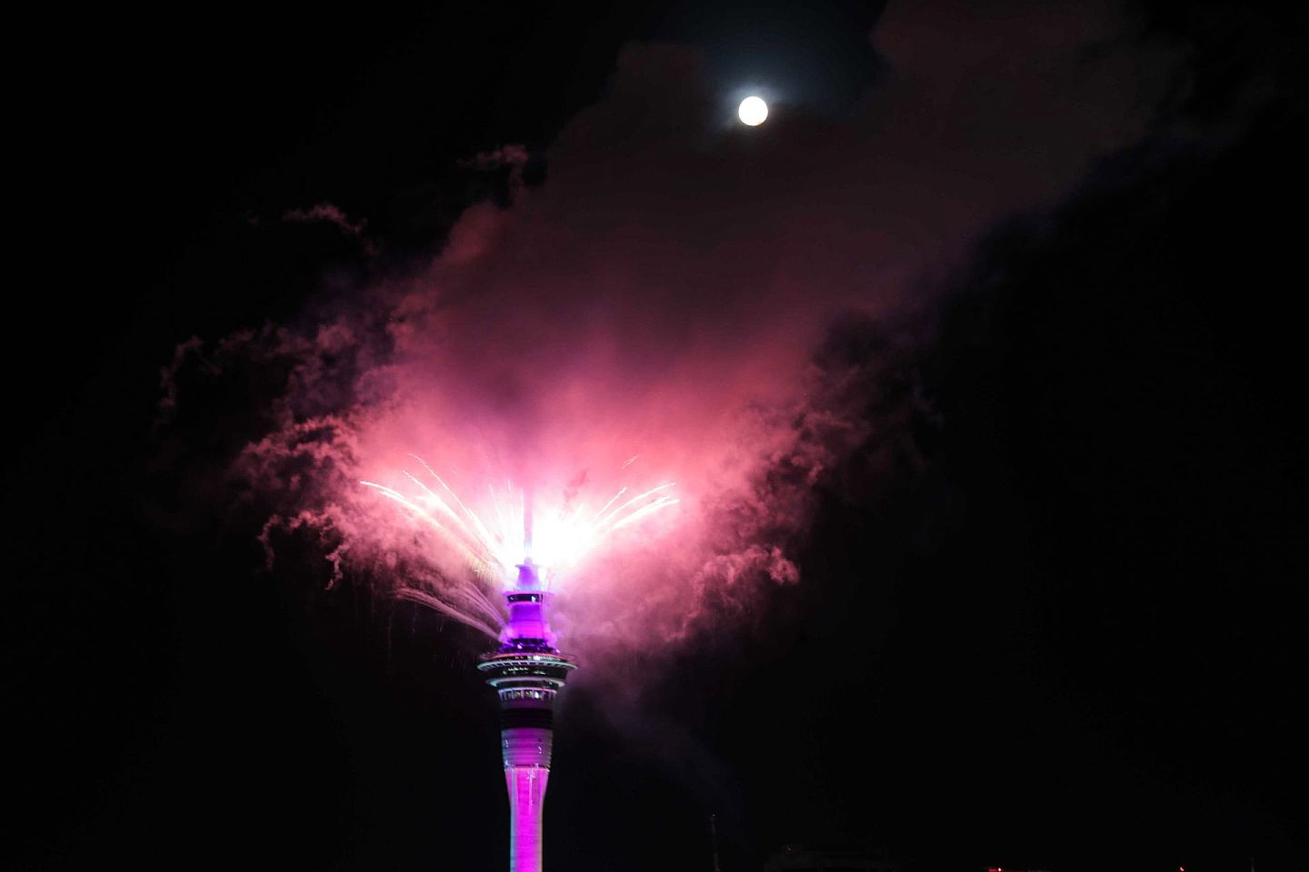 图为12月31日新西兰奥克兰天空塔发射烟花，与皎洁的月光相映成趣。（AP）