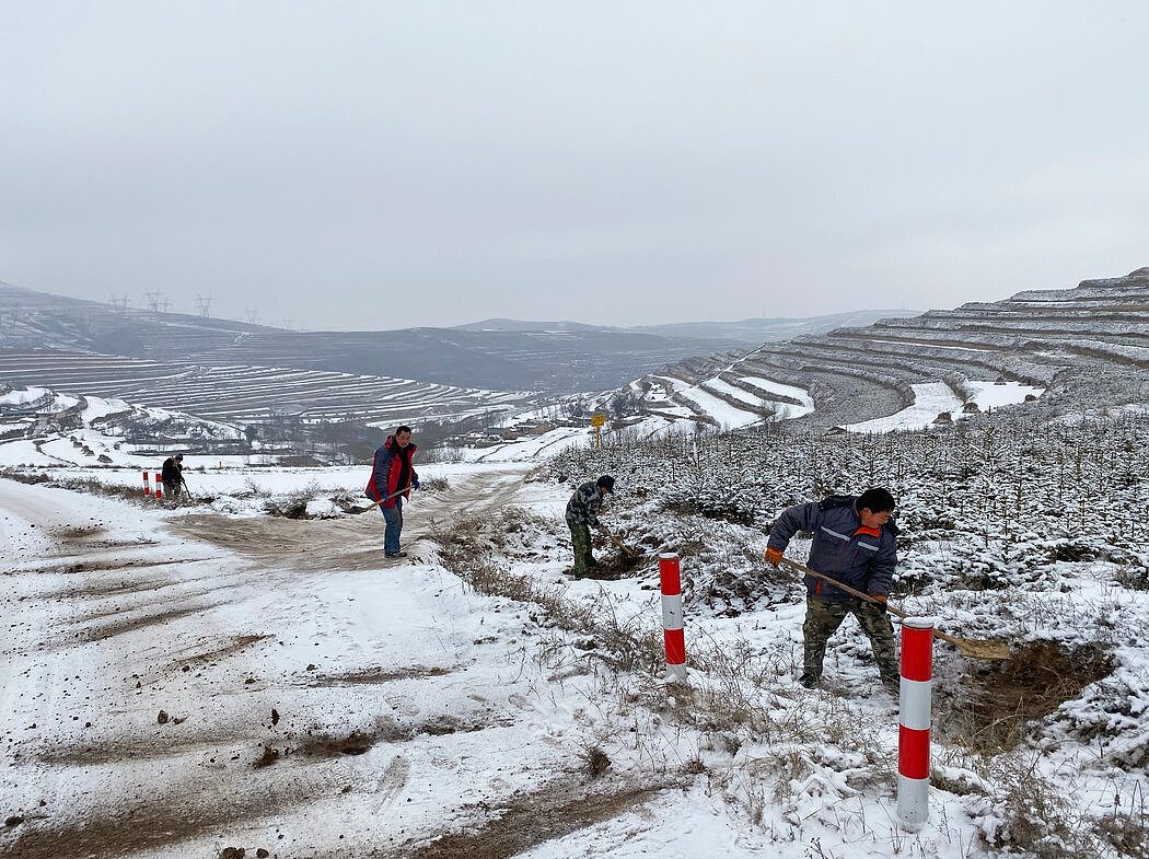 在甘肃省，建筑工人在一条偏远的山区村庄附近将泥土铲到道路上以增加附着力。这是中国扶贫计划的一部分。