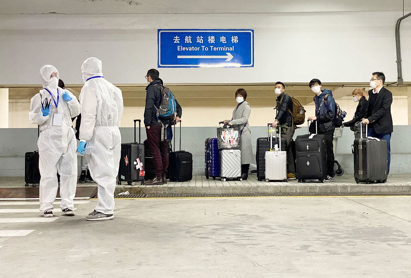 2020年3月19日，在上海浦东国际机场，工作人员引导入境人员等待乘坐转运车辆。（新华社）