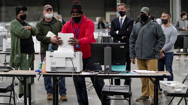 2021年1月5日，佐治亚州亚特兰大市佐治亚世界会议中心，富尔顿县的一名选举工作者在选举观察员注视下，将缺席选票放入扫描仪中。