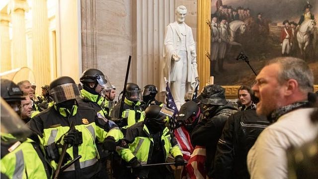 暴力事件是在美国历史人物和场景的超现实背景下发生（图为警察在国会大厦内的亚伯拉罕·林肯雕像旁边与支持特朗普的暴徒对峙）。