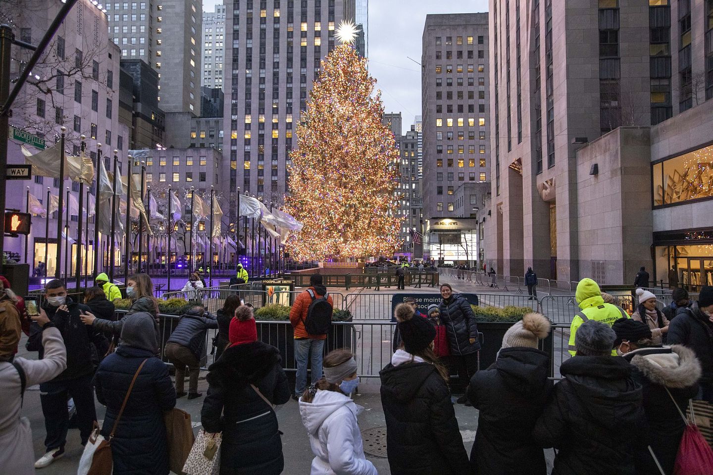 2020年12月22日，人们在美国纽约的洛克菲勒中心与圣诞树合影。为防止人群聚集，今年洛克菲勒圣诞树不对游客近距离开放，只可在指定区域“远观”。（新华社）