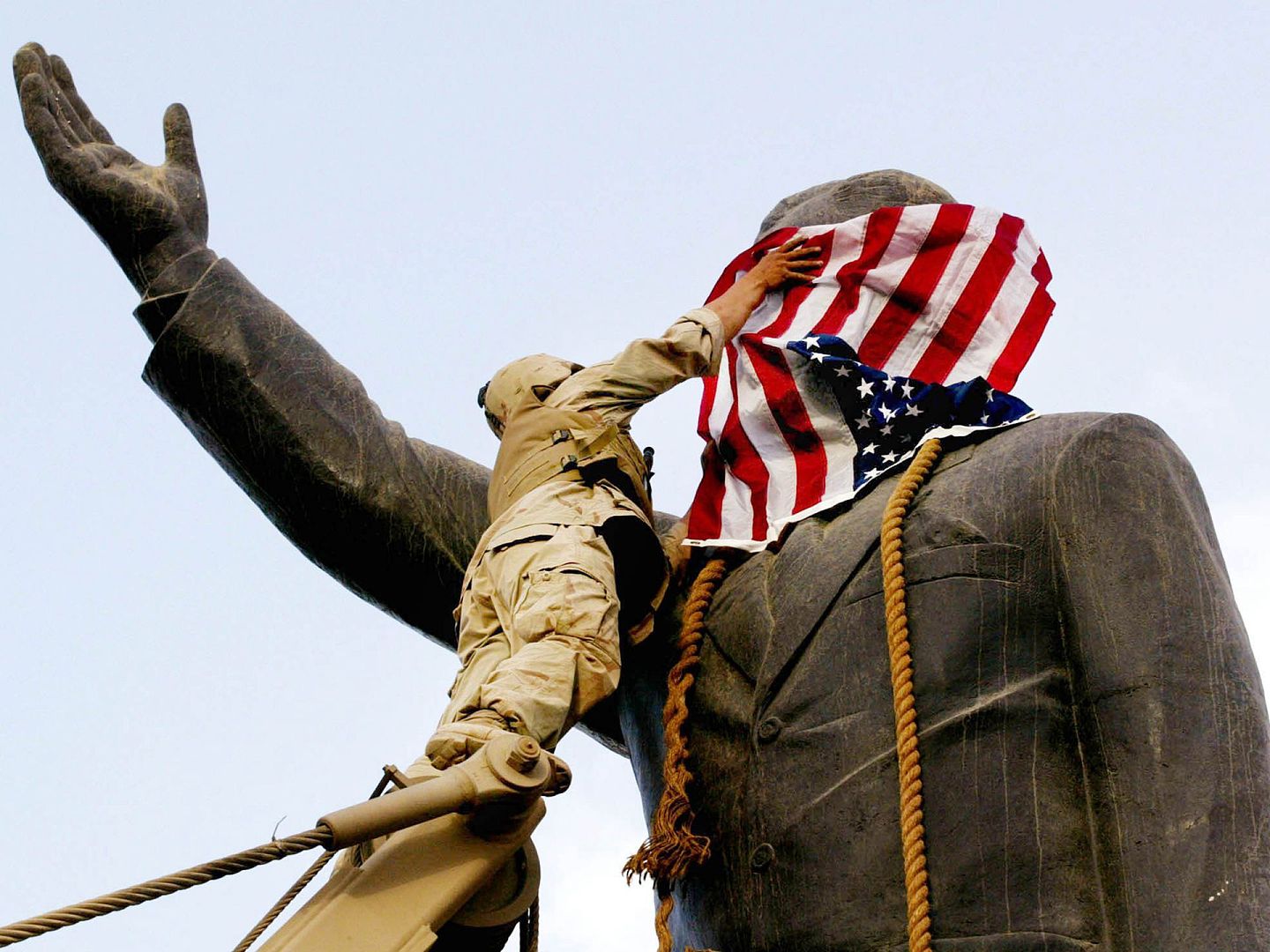 经过激战，美英联军击败伊拉克军队。图为一名士兵用美国国旗挡住萨达姆雕像的头部。（VCG）