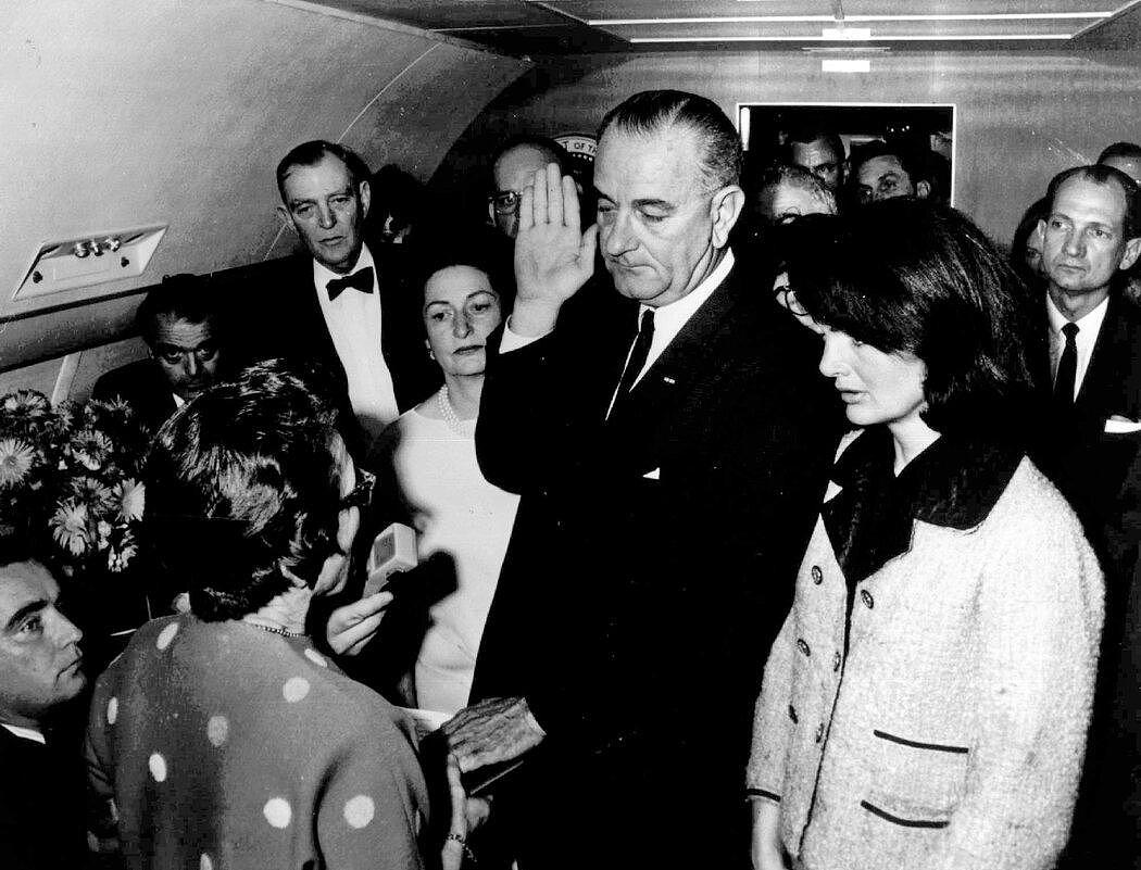 1963年11月22日，约翰·F·肯尼迪总统遇刺后，林登·B·约翰逊在总统专机上宣誓就任总统。右侧是肯尼迪的遗孀杰奎琳·肯尼迪。