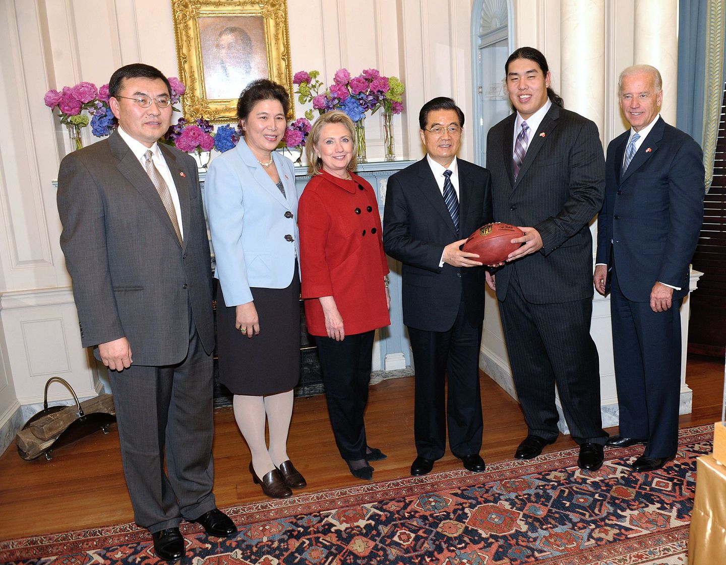 2011年1月19日，胡锦涛抵达美国的第一次正式欢迎午宴上，美国职业橄榄球联盟（NFL）华裔新星王凯（Ed Wang）手持橄榄球出席。拜登、时任国务卿希拉里（Hillary Clinton）以及王凯的父母Robert 和Nancy在旁边。（新华社）