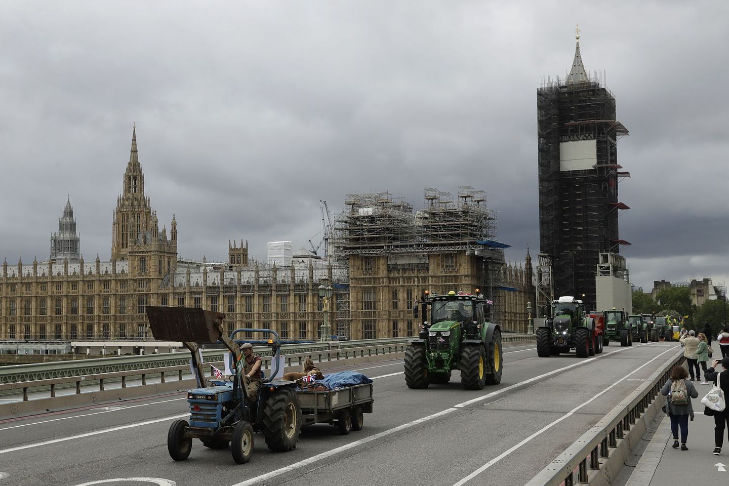 2020年7月8日，在伦敦，“拯救英国农业”组织的农民驾驶拖拉机穿过议会大厦前的威斯敏斯特桥和脚手架搭成的大本钟，抗议英国脱欧后从美国进口廉价食品。（AP）
