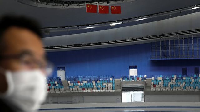 A media member wearing a face mask following the coronavirus disease (COVID-19) outbreak is seen near Chinese flags at National Speed Skating Oval, a venue of the 2022 Winter Olympic Games, during an organised media tour in Beijing, China January 22, 2021.