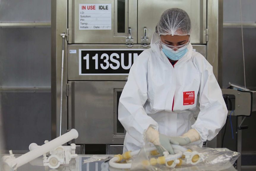 A woman in a hairnet, mask and protective suit holding plastic pipes in a lab