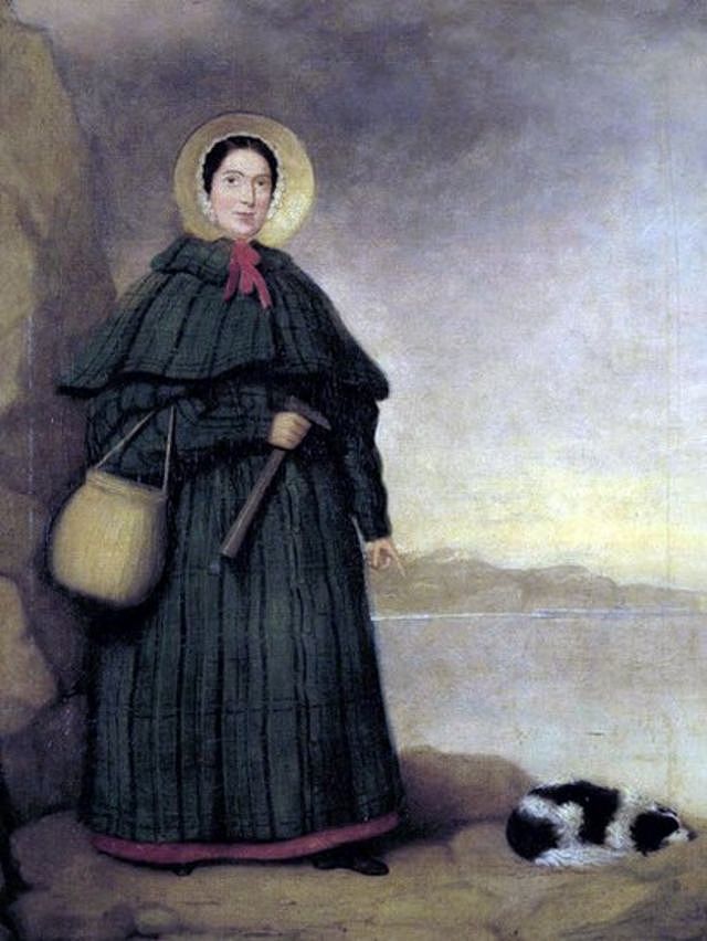 A portrait of Mary Anning donning a cape and bonnet. She's holding a hammer and a basket for her fossils, and her dog Tray is asleep at her feet.