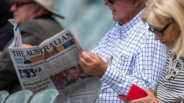 Man reads newspaper next to woman on phone
