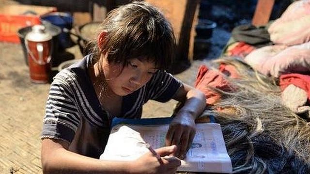 在云南省怒江州福贡县木克基村，一名孩子趴在床上做作业，她的家里没有桌子。