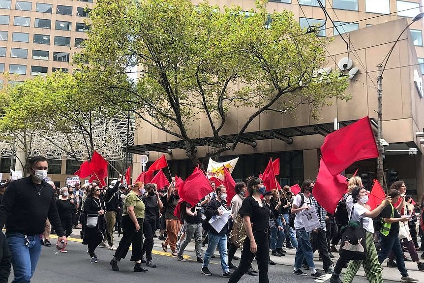 一群人挥着红旗在墨尔本的科林斯街上走着。