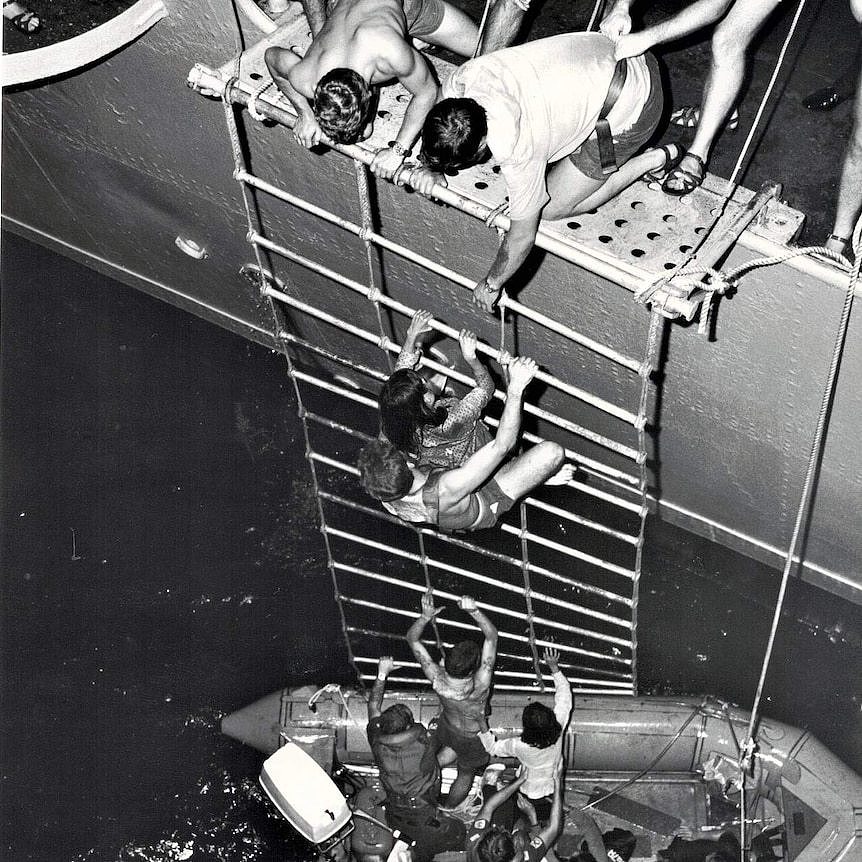 Vietnamese refugees rescued from the South China Sea, climbing up a roped ladder into a HMAS vessel.