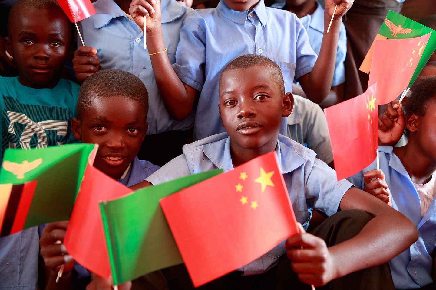2019年6月13日，在赞比亚卢萨卡省琼圭区，手持中赞两国国旗的儿童参加中国援非“万村通”赞比亚项目竣工仪式。“万村通”项目是2015年中非合作论坛约翰内斯堡峰会提出的中非人文领域合作举措之一，旨在为非洲国家的1万个村庄接入卫星数字电视信号。（新华社）